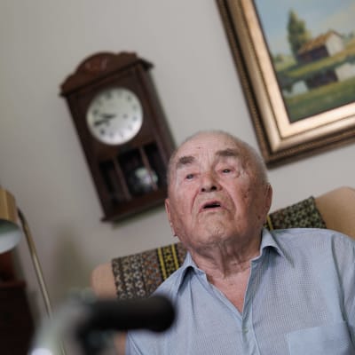 96-vuotias Aimo Rättyä katsoo televisiota kotinsa olohuoneessa. 