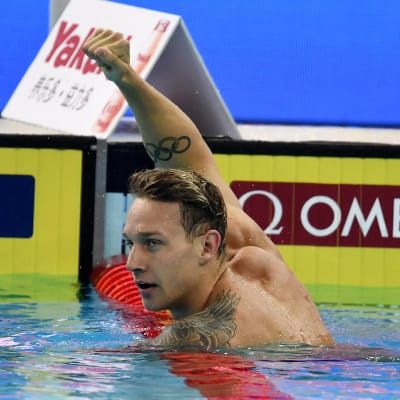 Caeleb Dressel höjer näven i luften i en simbassäng.