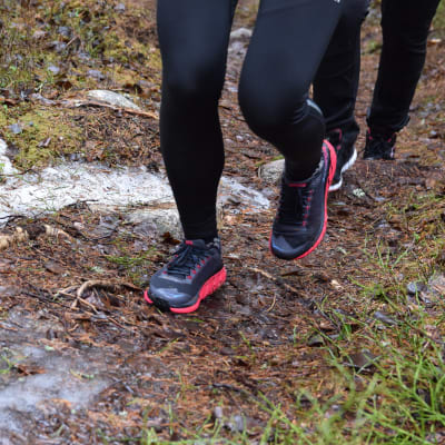 Närbild av fötter med gymnastikskor som pringer på en skogsstig med lite snö på.
