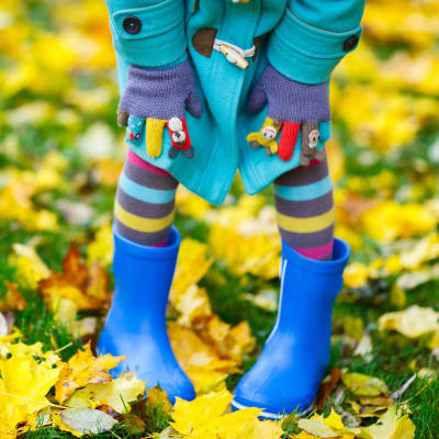 Ett barn med granna blåa stövlar och randiga strumpbyxor på en gräsmatta med gula löv.