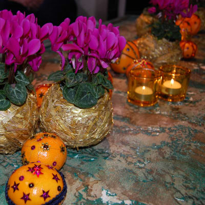 Ett bord som dekorerats med ceriserosa minicyklamenblommor, värmeljus i gula glaslyktor och mandariner och palesiner som dekorerats med paljetter och sidenband i olika mönster.