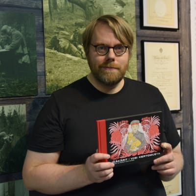 Sarjakuvataiteilija Mika Lietzén pitelee kädessään jääkäriliikkeen historiasta kirjoittamaansa sarjakuva-albumia.