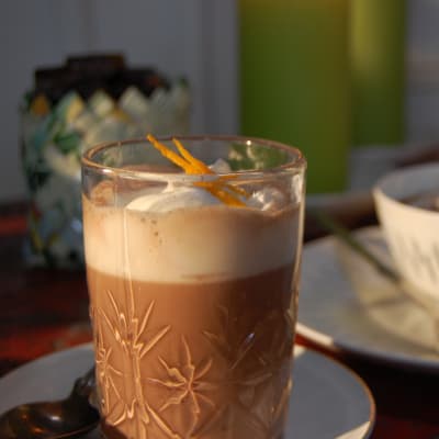 Ett glas med varm choklad toppat med vispgrädde och rivet apelsinskal.