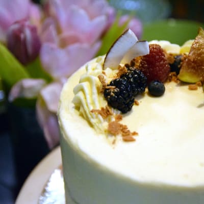 En tårta spacklad med ljus frosting och barnerad med björnbär, hallon, blåbär, fikon, kokosflarn och guldströssel.