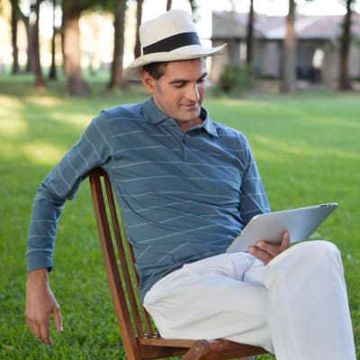 En man sitter ute och läser en e-bok. 