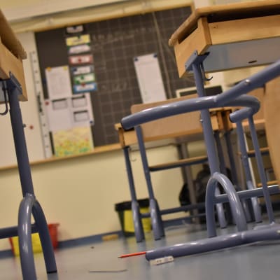 Kaadettu tuoli ja levinneet työvalineet koulun luokassa