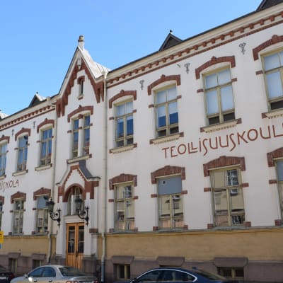 Skolbyggnaden på Smedsgatan 2. Den har en vit fasad med röda tegeldekorationer på fönstren.