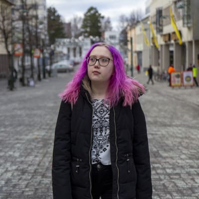 En kvinna med rosa hår och svart jacka. Går på en gågata i Jakobstad. 