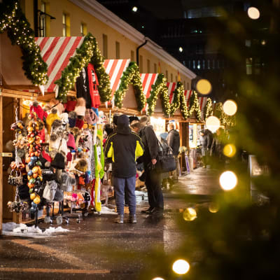 Internationella julmarknaden i Helsingfors. Juliga små försäljningsstånd och kunder som tittar på varor med ryggen mot kameran.
