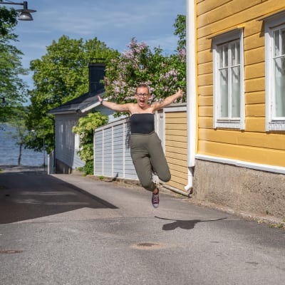 Malin Valtonen hoppar och ser glad ut på en gata, omringad av äldre hus.