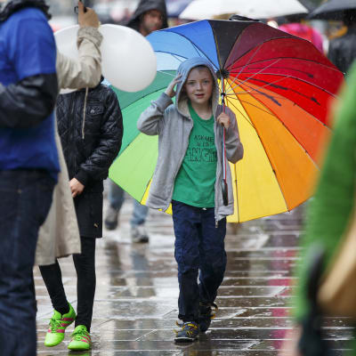 En pojke håller i ett regnbågsfärgat paraply medan han går ute i regnet.