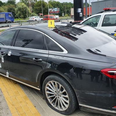 en svart bil står parkerad på en parkeringsplats. Bilen har flera skotthål.
