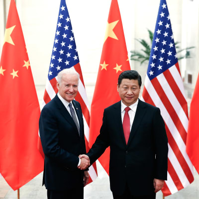 Joe Biden och Xi Jinping skakar hand. I bakgrunden USA:s och Kinas flagga.