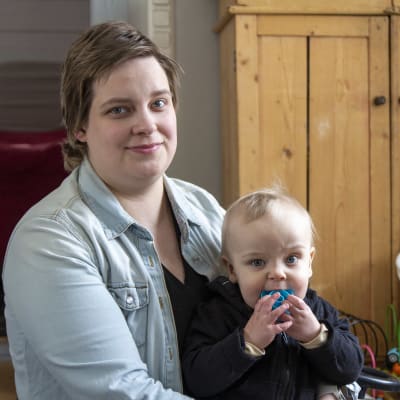 En kvinna som sitter på golvet i sitt vardagsrum, med ett litet barn i famnen.