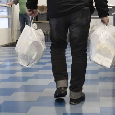 En man bär på två vita plastkassar med mat.