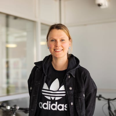 En kvinna tittar leende in i kameran. I bakgrunden ser man parkerade cyklar.