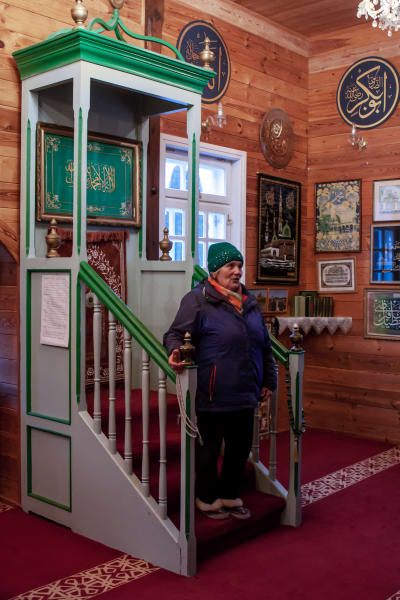 En äldre kvinna i stickad mössa står inne i ett moskérum.