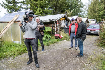 Kuvassa neljä miestä kuvaa videokameralla pihamaalla Koskenkorvalla, taustalla taloja, metsää, auto.