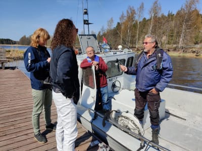 Två män står i en båt och två kvinnor på en brygga och pratar med varandra.