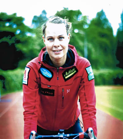 Henrika Backlund ser rakt mot kameran. Hon sitter på en cykel och är iklädd en röd träningsjacka.