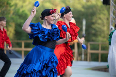 Färgsprakande dansare i blå och röd klänning i pjäsen Spamalot på Raseborgs sommarteater