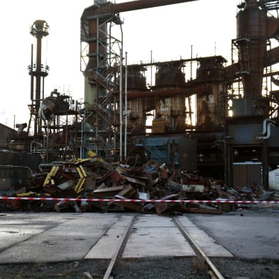 En person står och tittar på en hög med bråte framför en gammal stålfabrik.