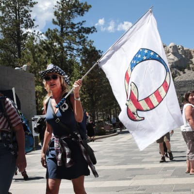 Qanon-protest i USA. En kvinna viftar med en flagga som har ett Q på sig. Bokstaven är färgad i USA:s flaggas färger.