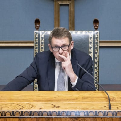 Matti Vanhanen i pampig talmansstol i riksdagen, med handen mot kinden.