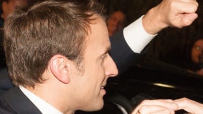 Frankrikes president Emmanuel Macron i profil. Han ler och höjer näven som i hälsning.