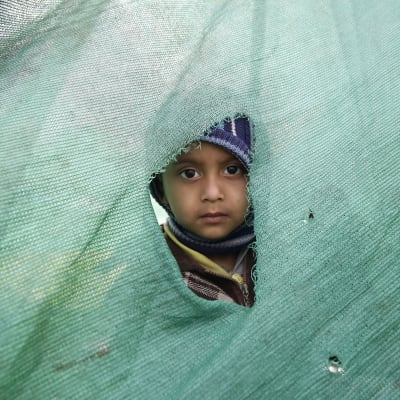 Flicka kikar ut genom söndrigt tält i Katmandu.