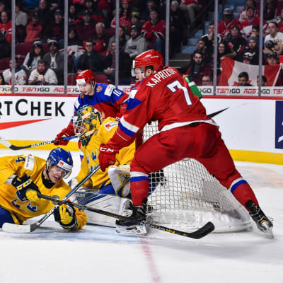 En svensk spelare ligger på isen framför eget mål. En rysk spelare försöker peta in pucken.