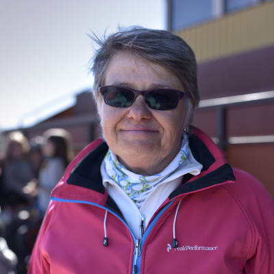 en kvinna med solglasögon och sportiga kläder ser mot kameran i publikläktaren på en idrottsbana