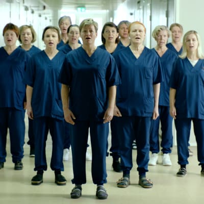 En grupp sjungande vårdare fotograferade i en sjukhuskorridor.