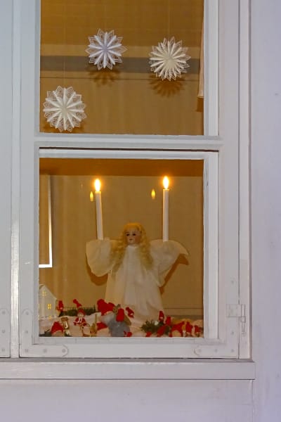 Ett fönster dekorerat med julprydnader i ett trähus