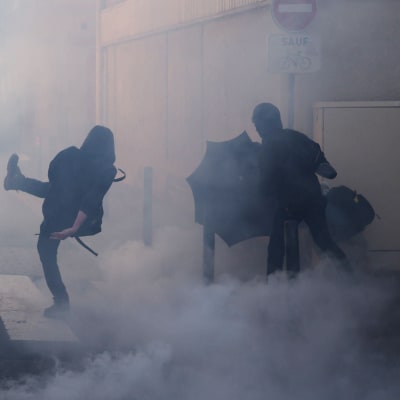 Demonstranter kastar sten i ett moln av tårgas.