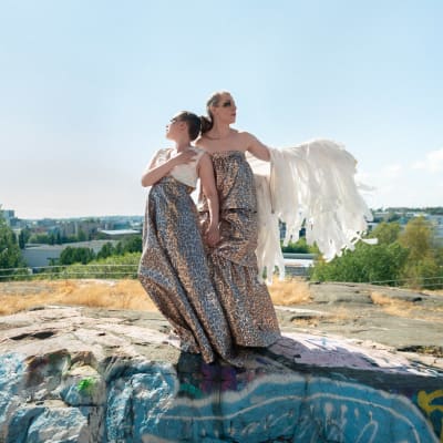 Marja Ahlsved och Heidi Kiviharju från Arosa Ensemble står iklädda klänningar på en klippa i en stad.