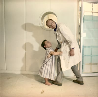 Valkotakkinen mies ja tämän takista kiinni pitävä lyhytkasvuinen mies seisovat vaaleassa tilassa, kuva elokuvasta Solaris.