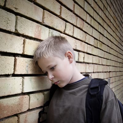 Nedstämd pojke som lutar sig mot väggen. 