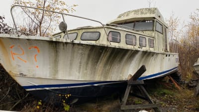 En gammal stor och smutsig motorbåt på några träbockar på land. 