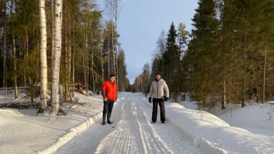 Två män på en skogsväg i vintrigt landskap. 
