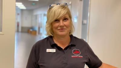 En kvinna med ett neutralt leende står i en dörröppning. 