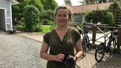 Nina Gustafsson med kameran i handen framför trädgården. 