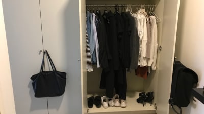 Svarta och gråa kläder hänger i en garderob. 