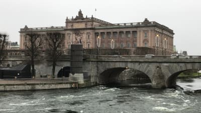 Sveriges riksdagshus med strömmen och bron i förgrunden.