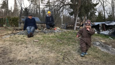 David och Victoria Grönlund sitter på en sten i trädgården och tittar på 2-åriga Ylva.