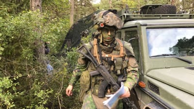Rekryt med grön målning i ansiktet och vapen på magen.