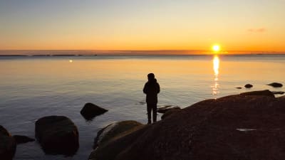 Ett barn står och fiskar i solnedgången på Varlaxudden.