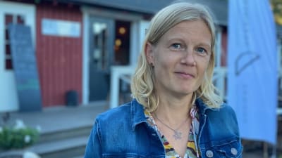 Ljushårig kvinna framför en cafébyggnad.