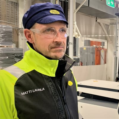 En man i reflexjacka och skyddsglasögon står intill en skärm i en fabrikshall