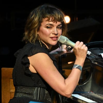 Norah Jones sitter vid ett piano och håller i en mikrofon.